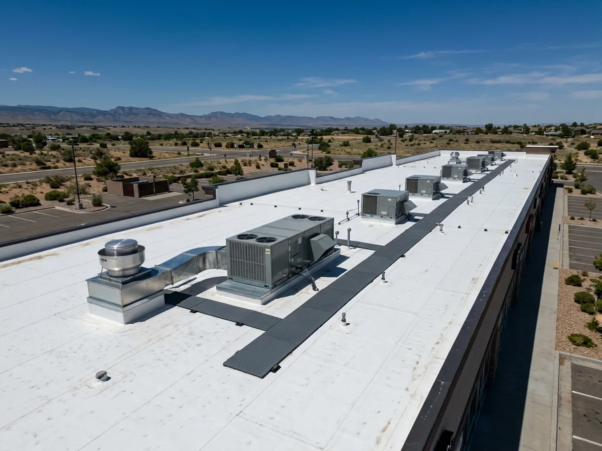 White TPO membrane roof over a single-story strip of shops, with rooftop air-conditioning units on curbs and a stainless kitchen exhaust fan