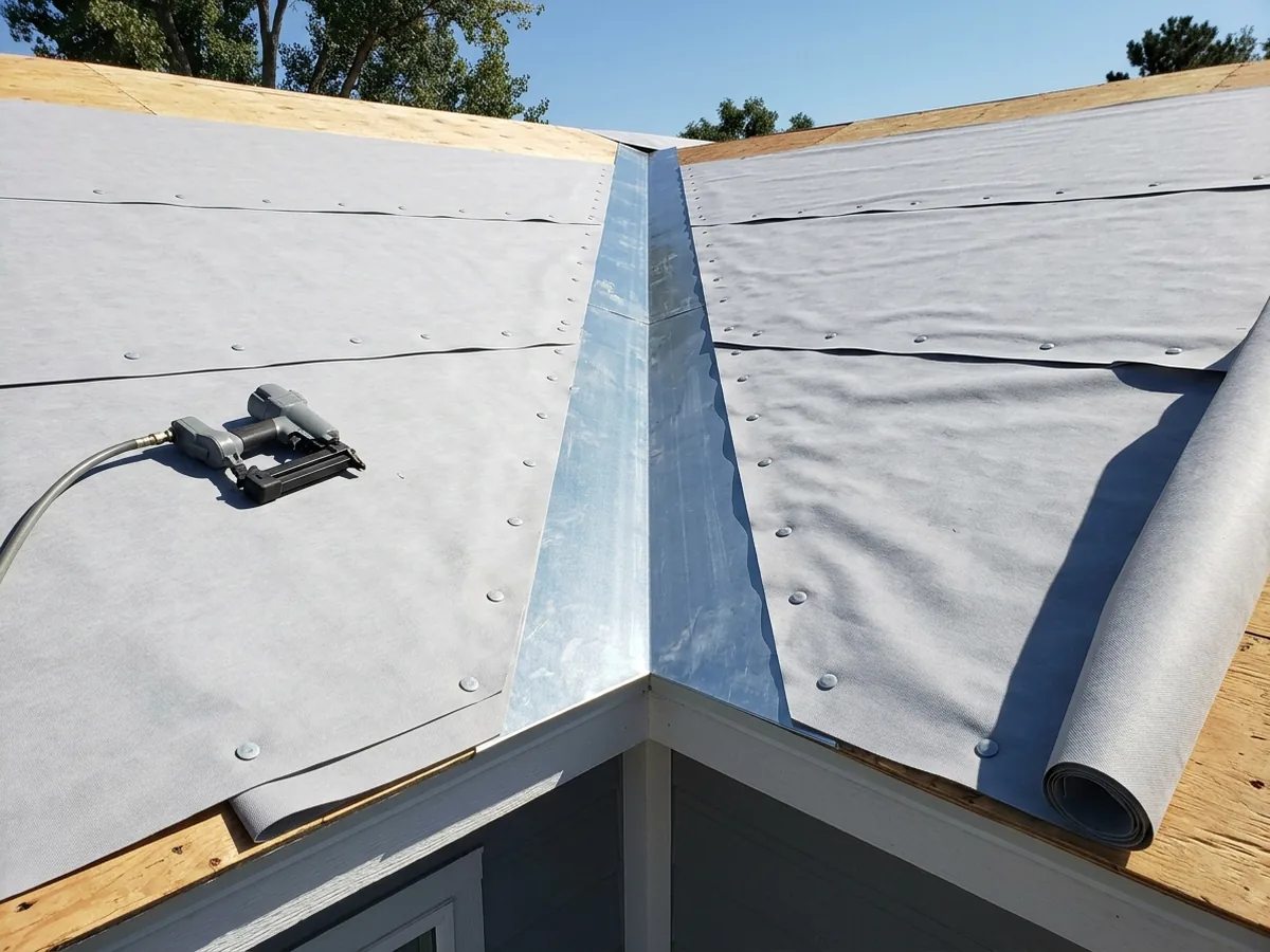 Gray synthetic underlayment rolled across a roof deck with a wide metal valley liner running down the center