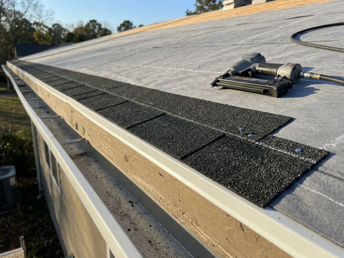 Row of starter strip shingles nailed along the eave edge of a roof over metal drip edge, before the first course